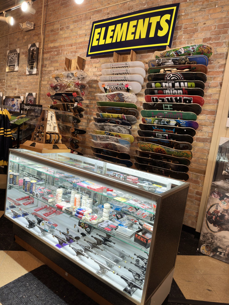 Deck wall under the yellow Elements sign, with a glass display case of trucks and wheels